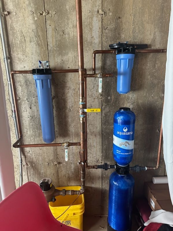 Water filtration system with copper pipes, blue filters, and a yellow bucket.