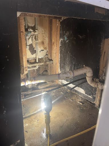 Interior view of exposed pipes and plumbing within a wall cavity, with a work light illuminating the area.