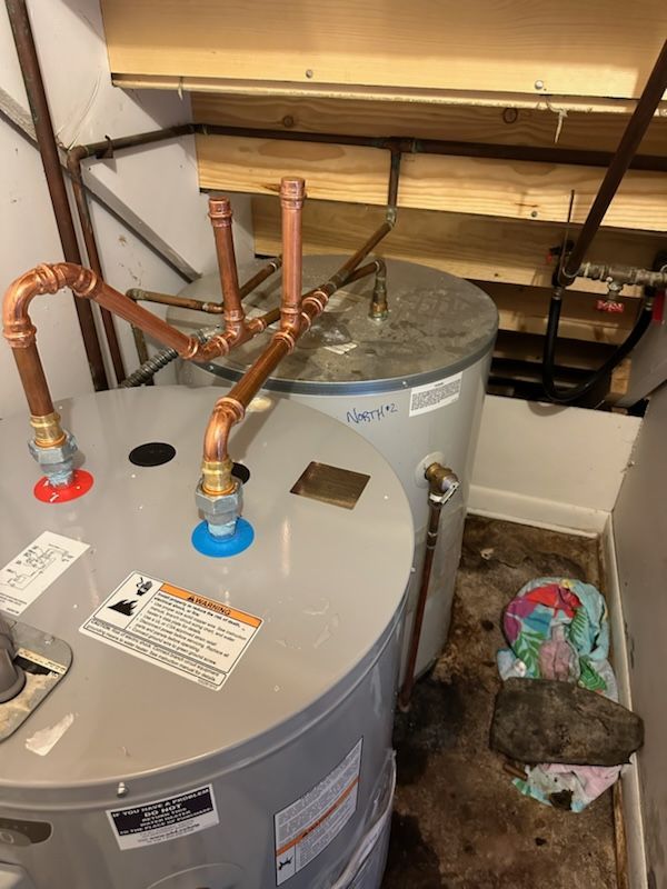 Two water heaters with copper pipes in a utility room.