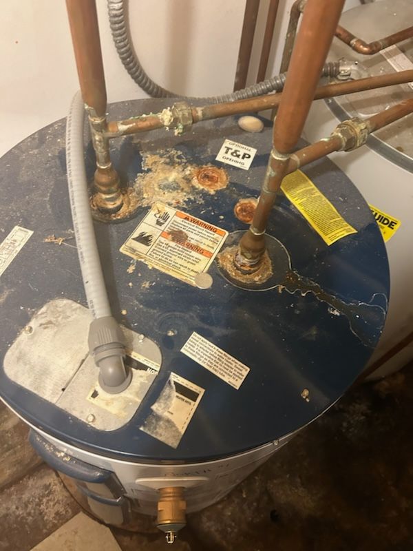 Water heater with corroded top, copper pipes, and a flexible gray drain hose.