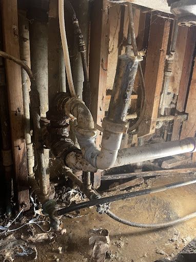 Pipes and plumbing in a wall cavity; corroded pipes, wood studs, and wet debris.