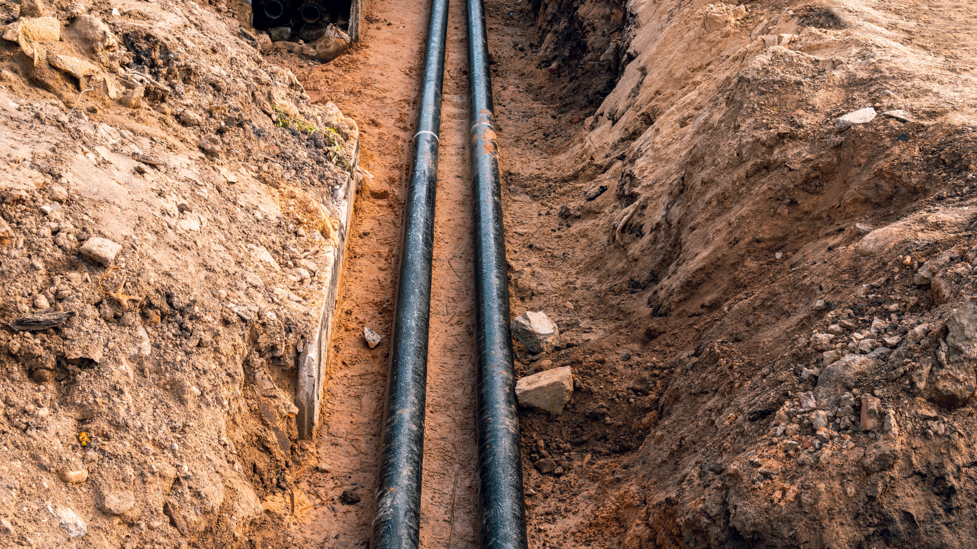 Two black pipes in a brown dirt trench.