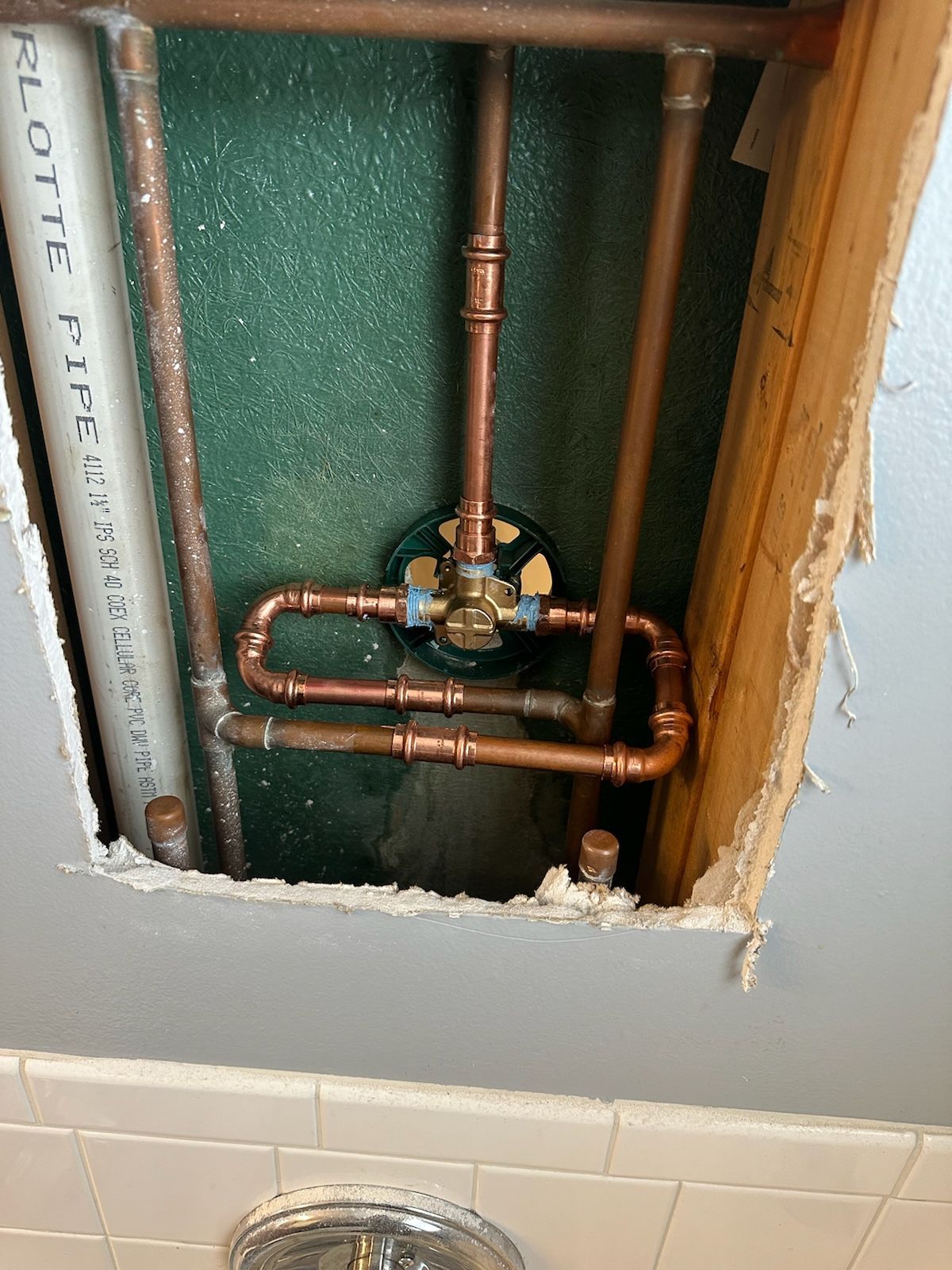Copper plumbing pipes with a mixing valve in a bathroom wall.