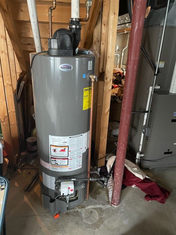 Gray water heater with copper and white pipes in a basement setting.