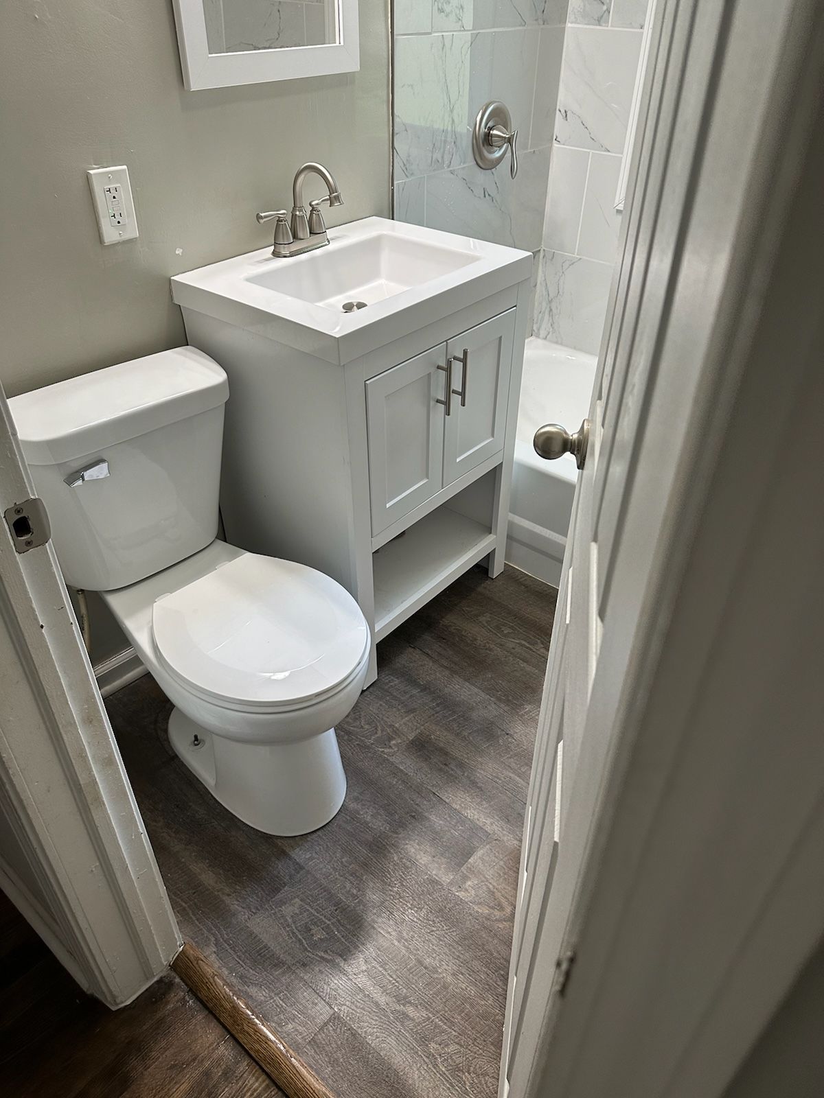 Small bathroom with white vanity, toilet, and bathtub; gray flooring.