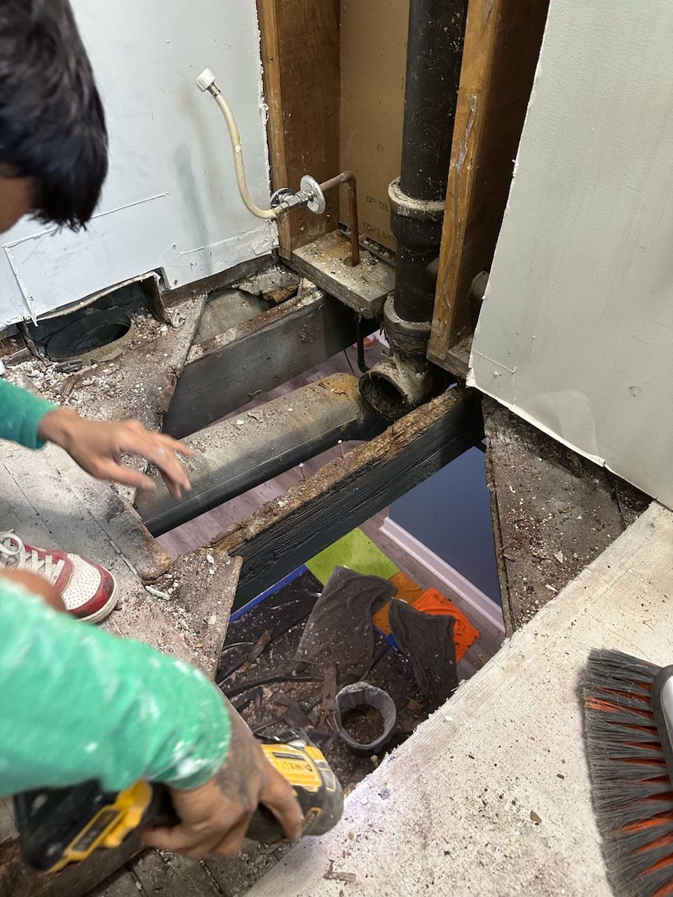 Person working on exposed bathroom floor and plumbing.