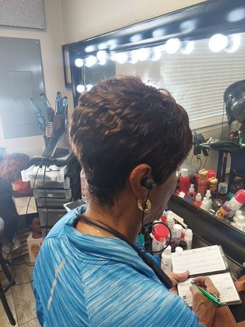 A woman in a blue shirt is writing in a notebook in front of a mirror.