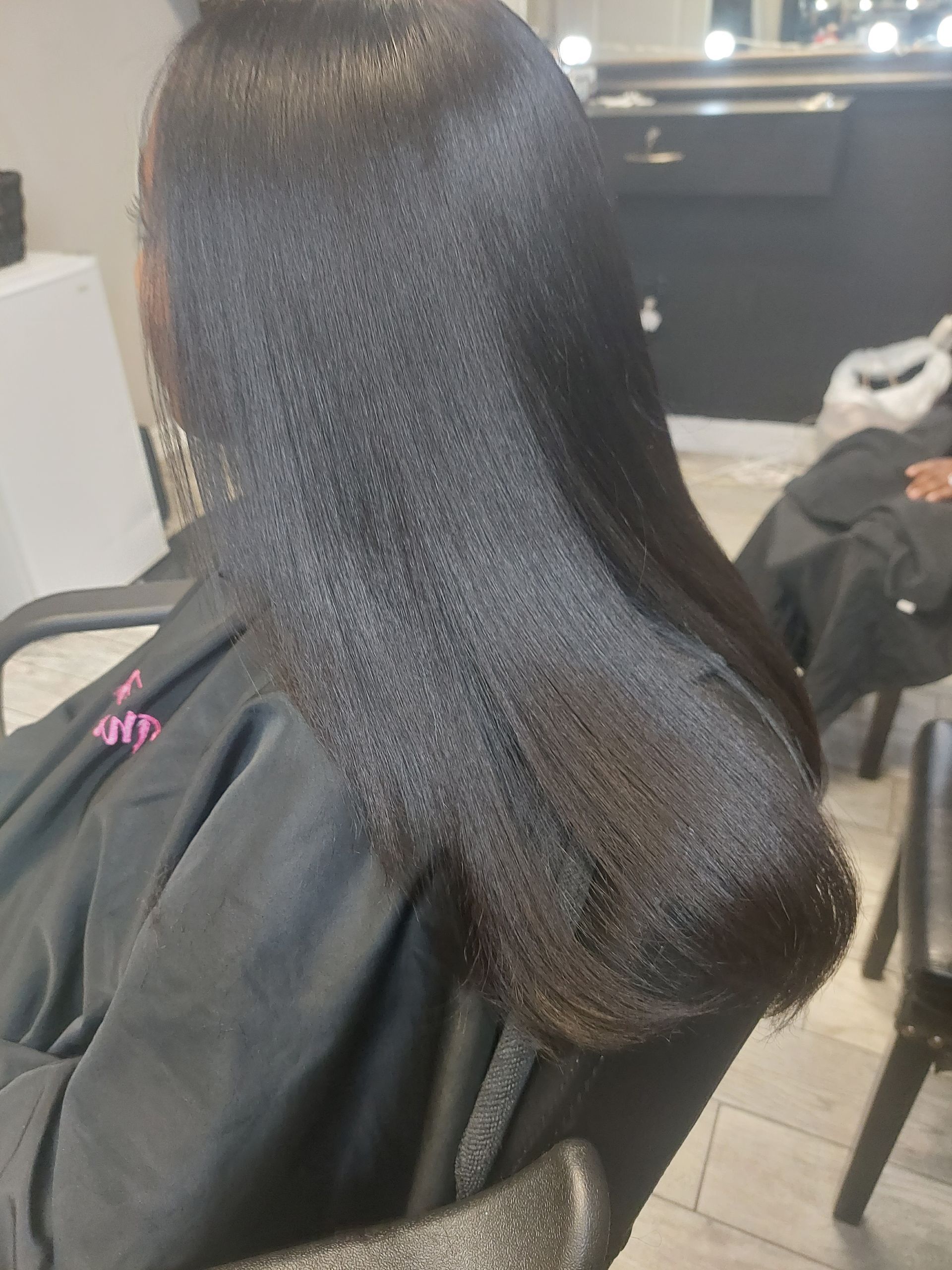 A woman is sitting in a chair with her hair straightened in a salon.