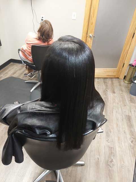 A woman with long black hair is sitting in a chair in a salon.