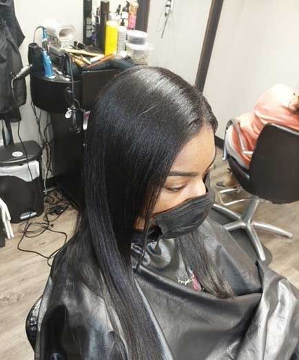 A woman wearing a mask is getting her hair cut in a salon.