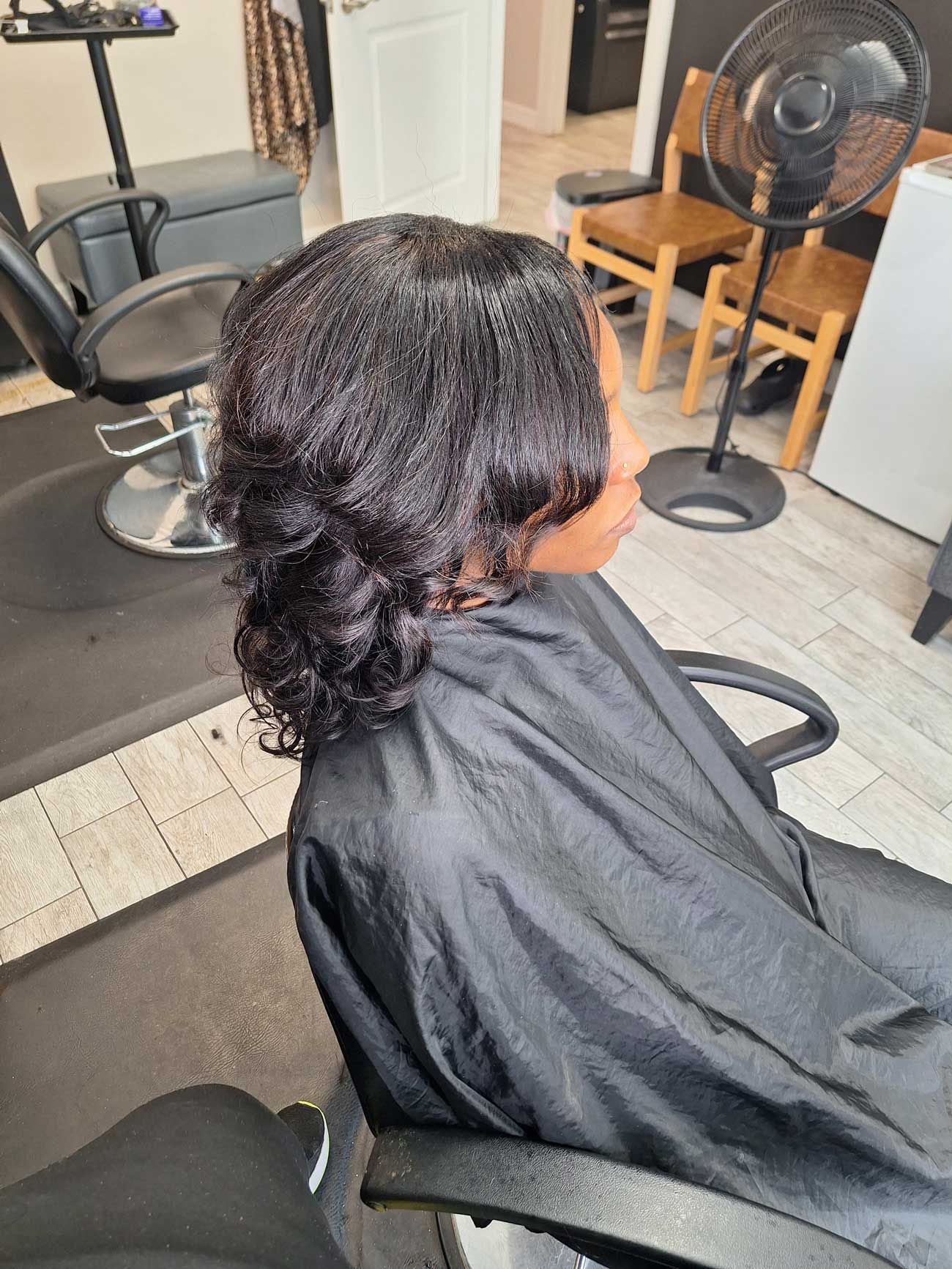 A woman is sitting in a chair in a salon getting her hair cut.