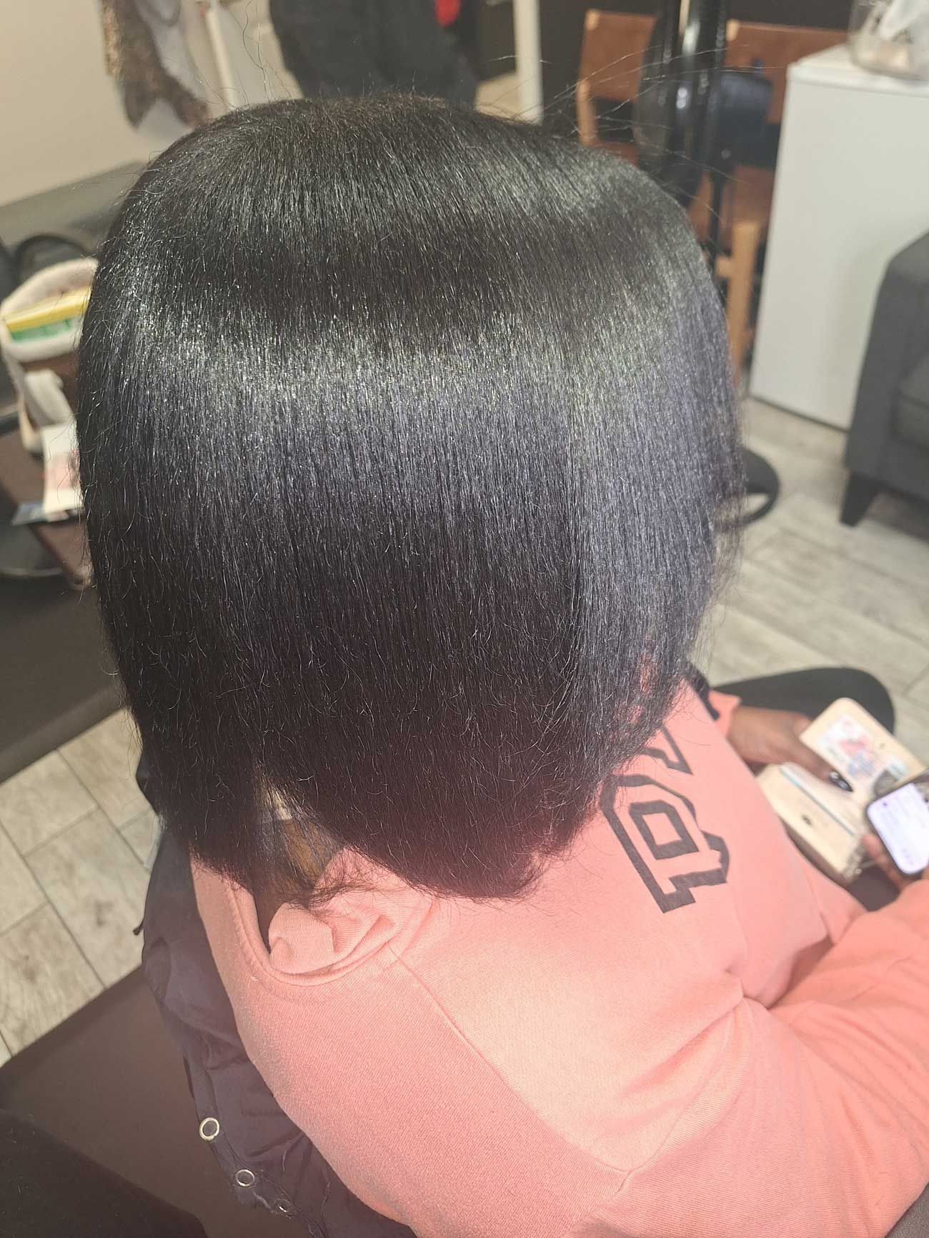 A woman is sitting in a chair with her hair straightened in a salon.