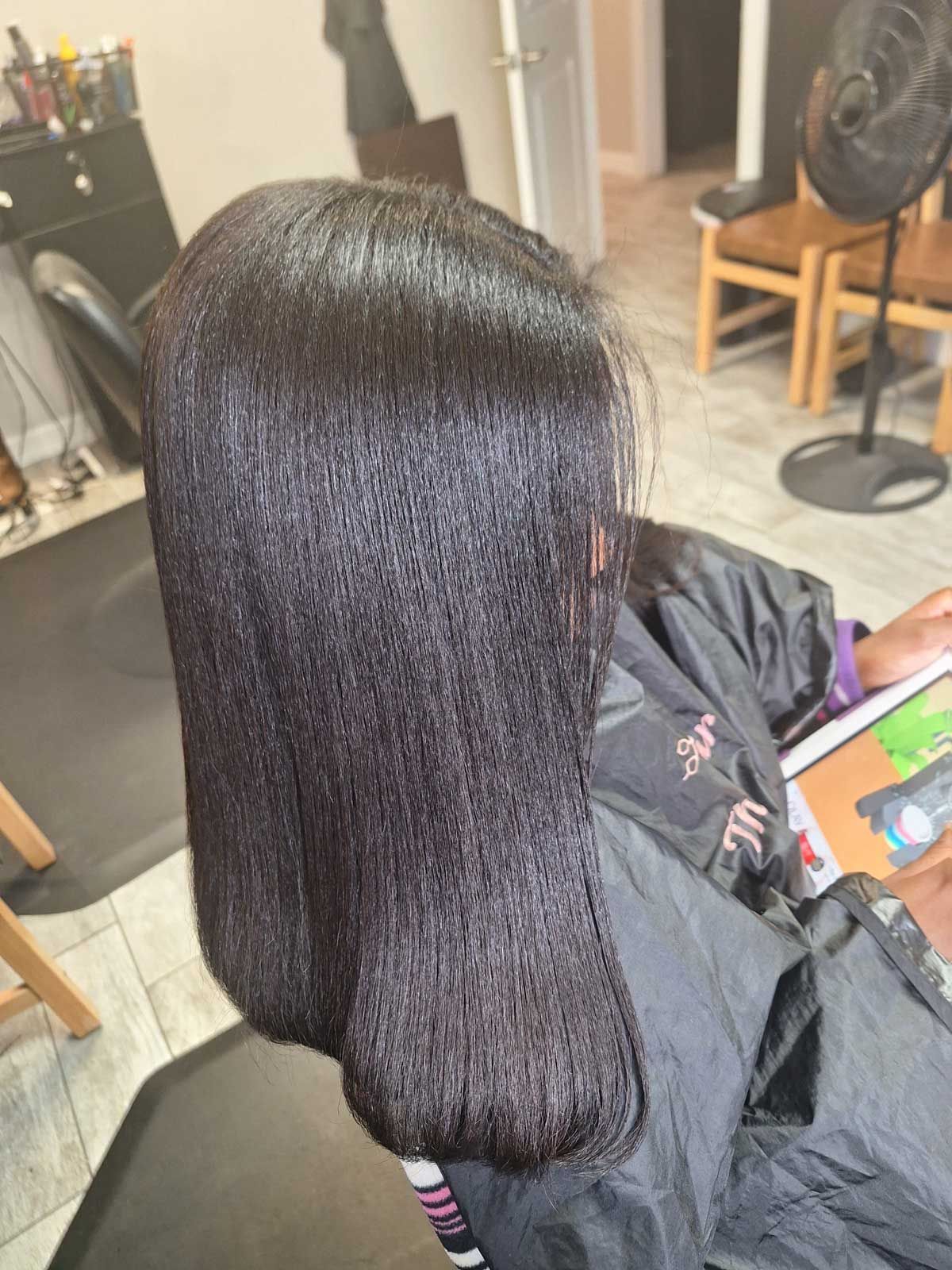 A woman is sitting in a chair with her hair straightened in a salon.