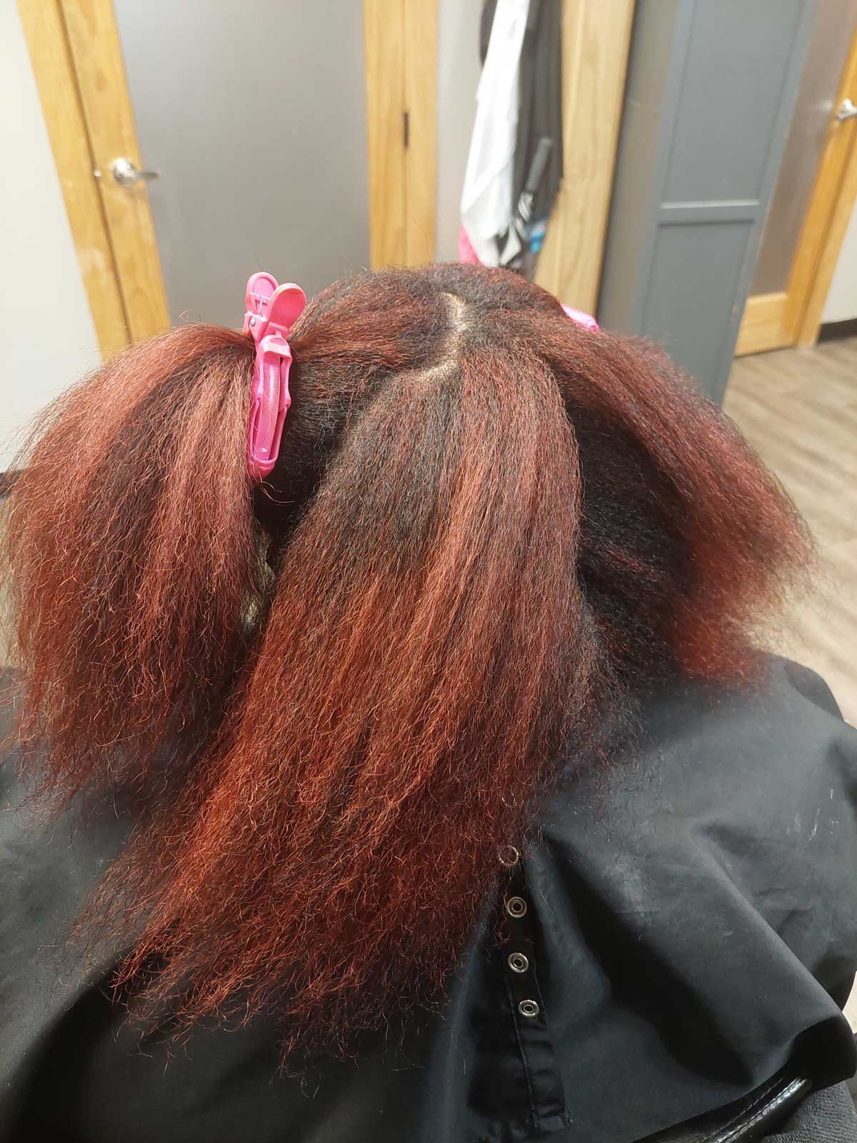A woman with red hair is sitting in a chair with clips in her hair.