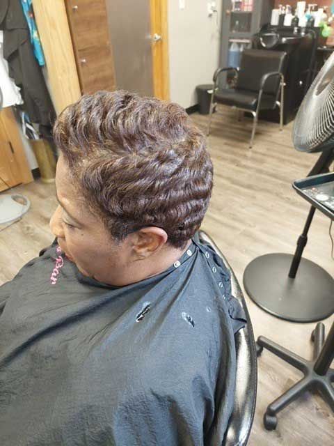 A woman is sitting in a chair in a salon getting her hair cut.