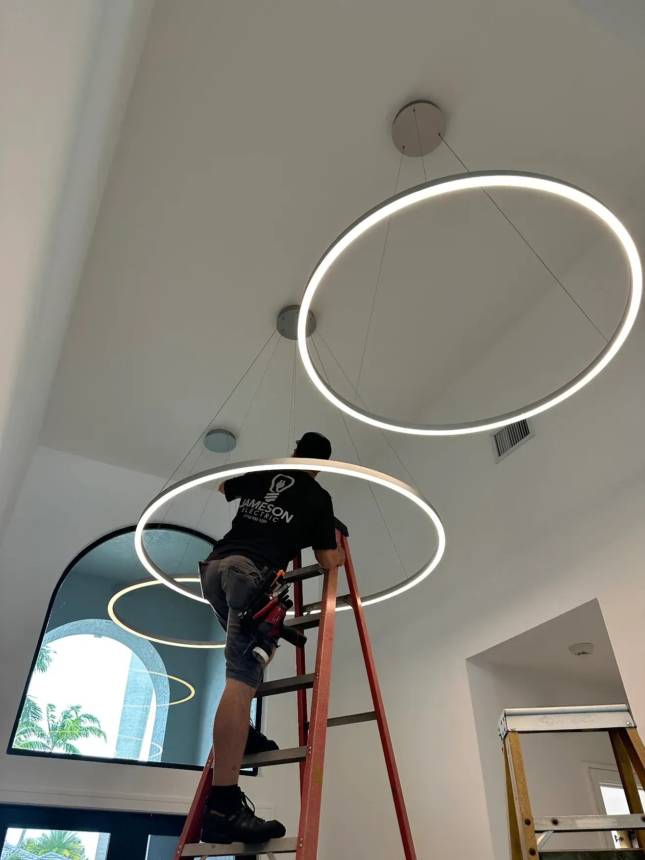 A man is standing on a ladder working on a ceiling light.