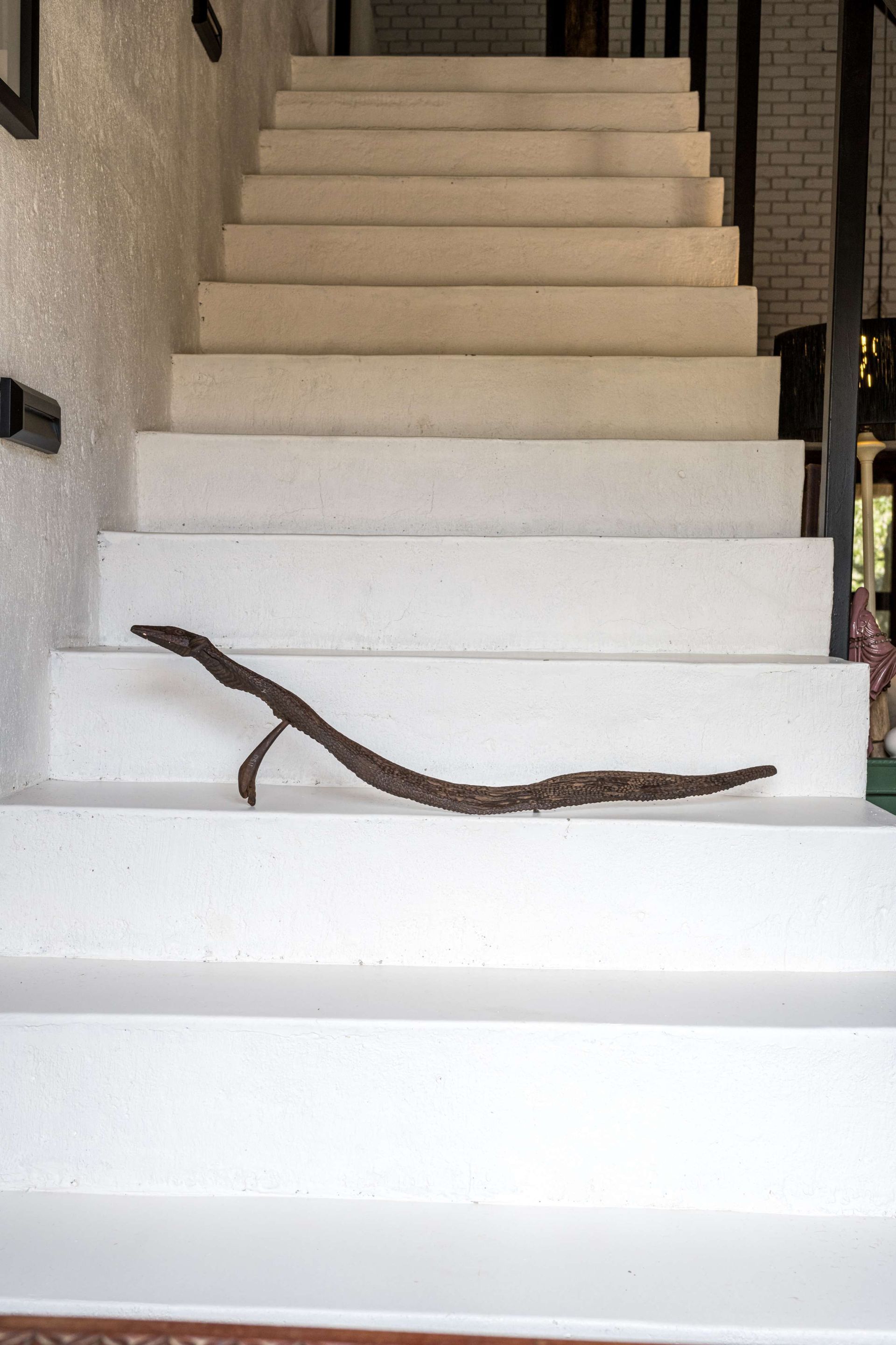 Serpent wood sculpture by Kenneth Nonyana showing intricate carved scales and detailed serpent head with dramatic curves against white stairs