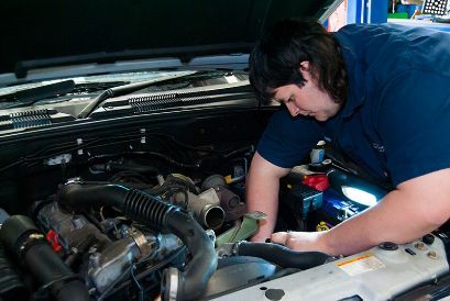 A Man in a Blue Shirt is Working on the Engine of a Car — Border Power Steering Service In Lavington, NSW