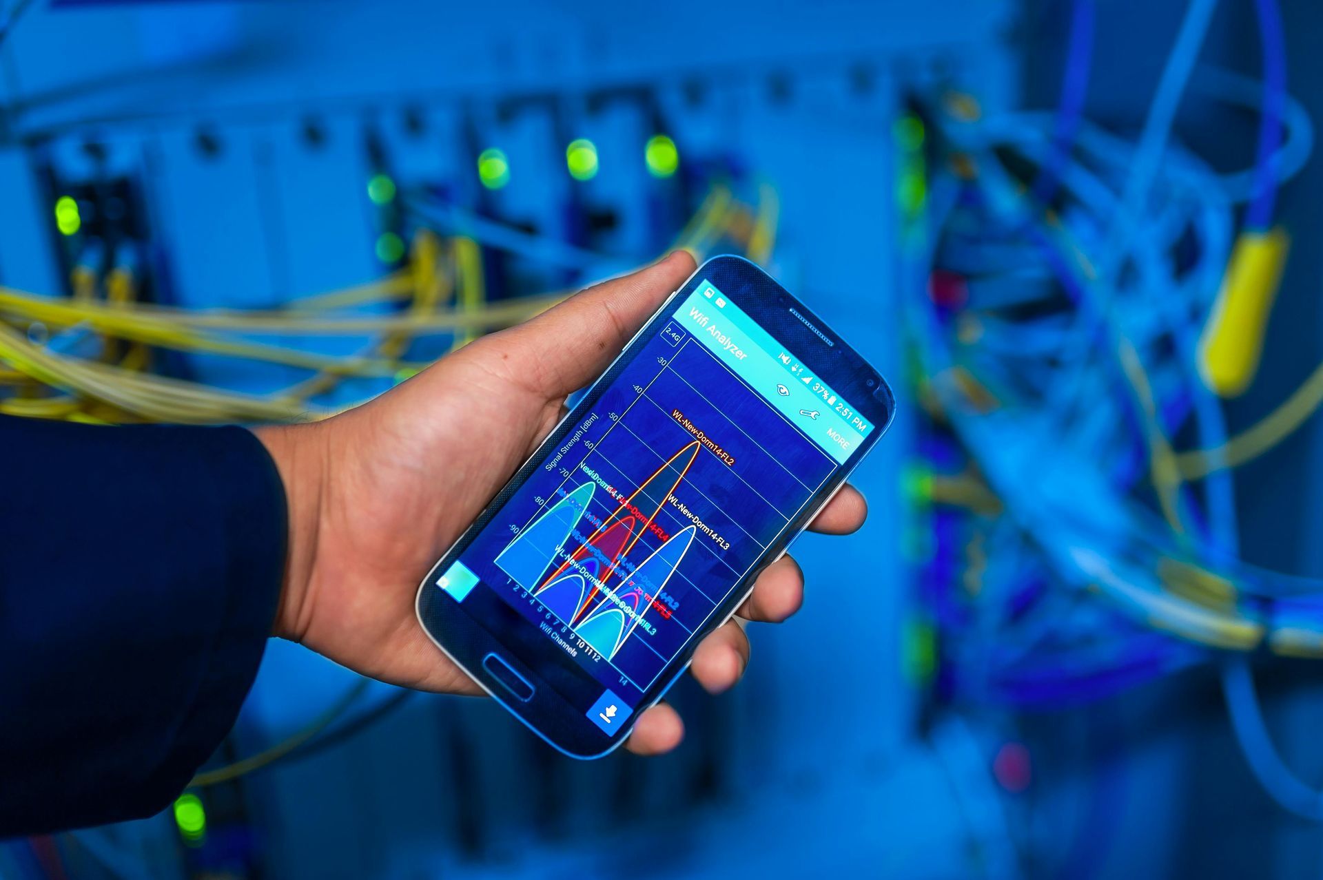 Hand holding a smartphone displaying data charts in a server room filled with colorful cables.