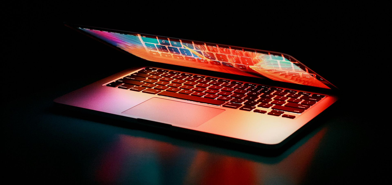 Open laptop with glowing, multicolored keyboard and screen against a black background.