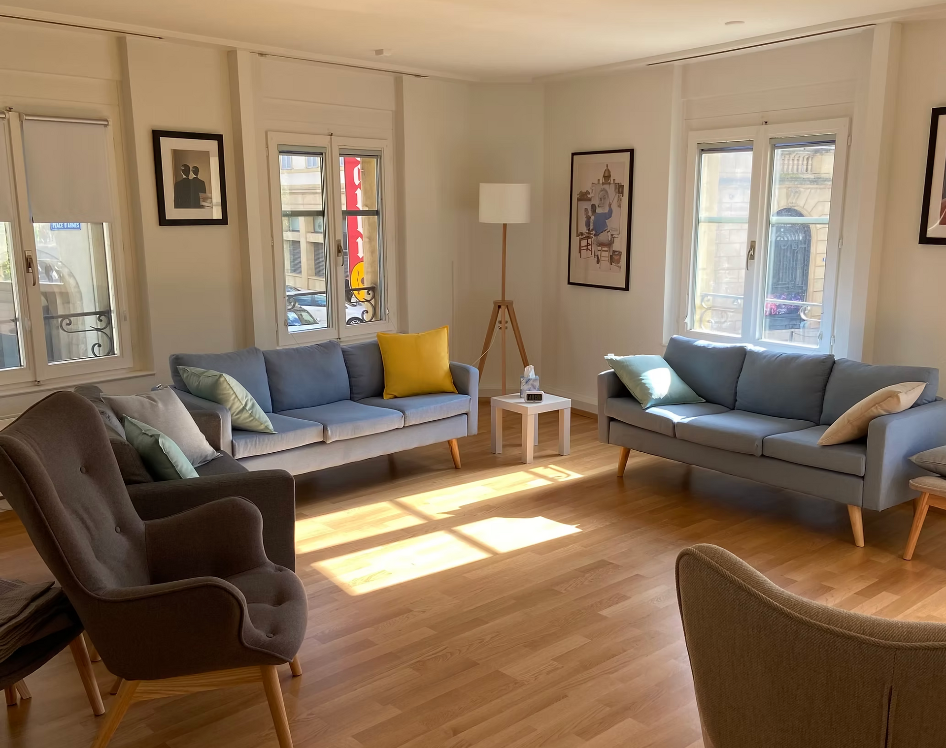 Salon spacieux avec canapés et fauteuils bleu clair, et parquet. La lumière naturelle inonde les pièces grâce aux fenêtres.