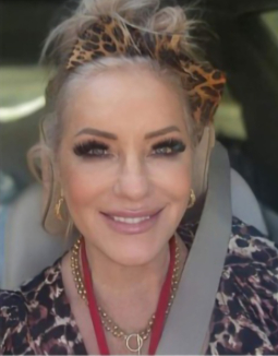 Woman with blonde updo, leopard print headband, smiling, wearing leopard print top, gold necklace.