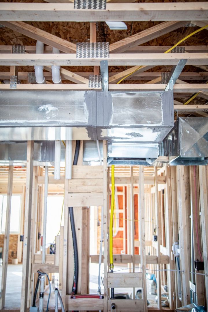 Interior of a building under construction, showing exposed wooden framing, ductwork, wiring, and plumbing.