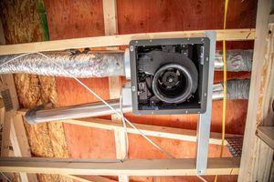Fan unit with ductwork installed in a wooden attic framework.