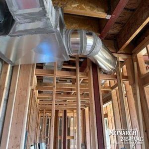 HVAC ductwork installation in a new home's wood frame, with silver metal duct and connecting flexible tube.