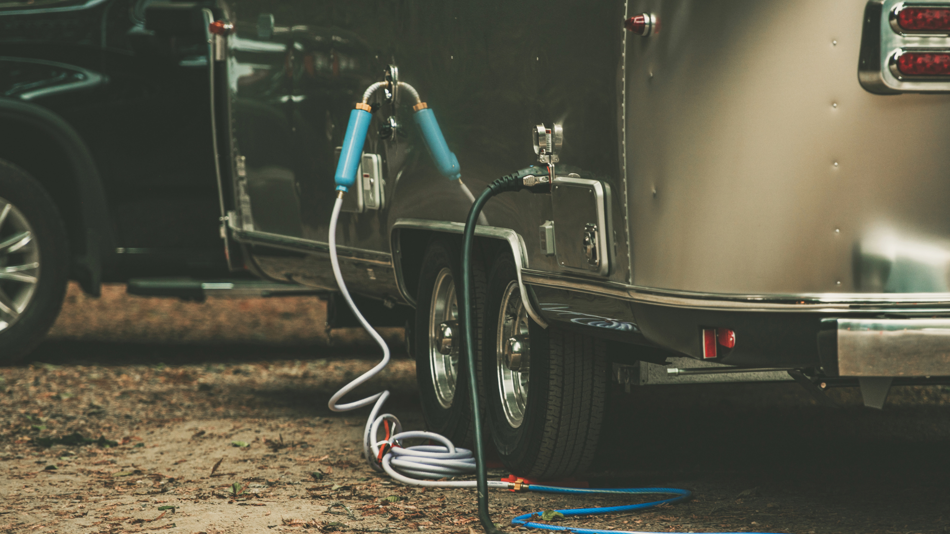 Silver camper trailer with water hose and electrical cord connected.