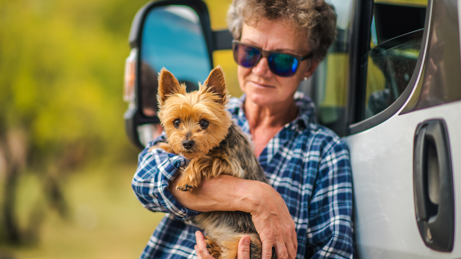 Woman holding a small dog next to a campervan. Both look toward the camera.