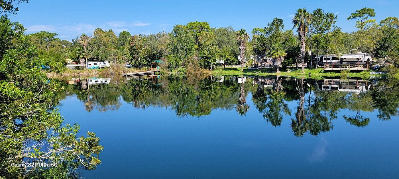 A calm, blue lake reflects the surrounding green trees and a clear blue sky.