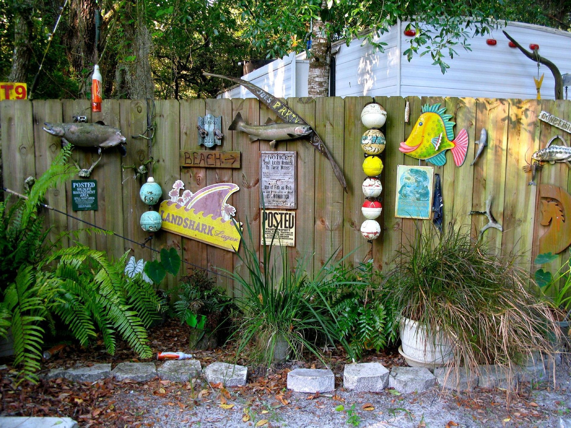 Wooden fence decorated with fishing-themed items, surrounded by plants and a gravel walkway.