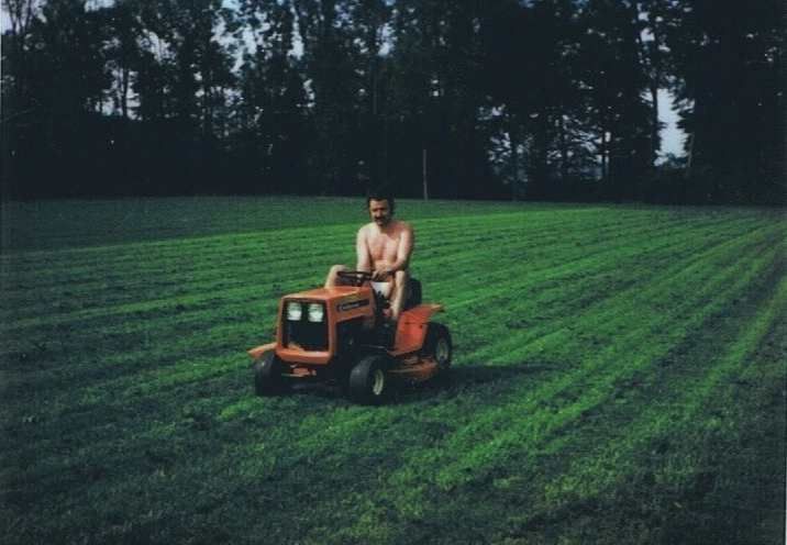 Un homme torse nu conduit une tondeuse à gazon dans un champ herbeux