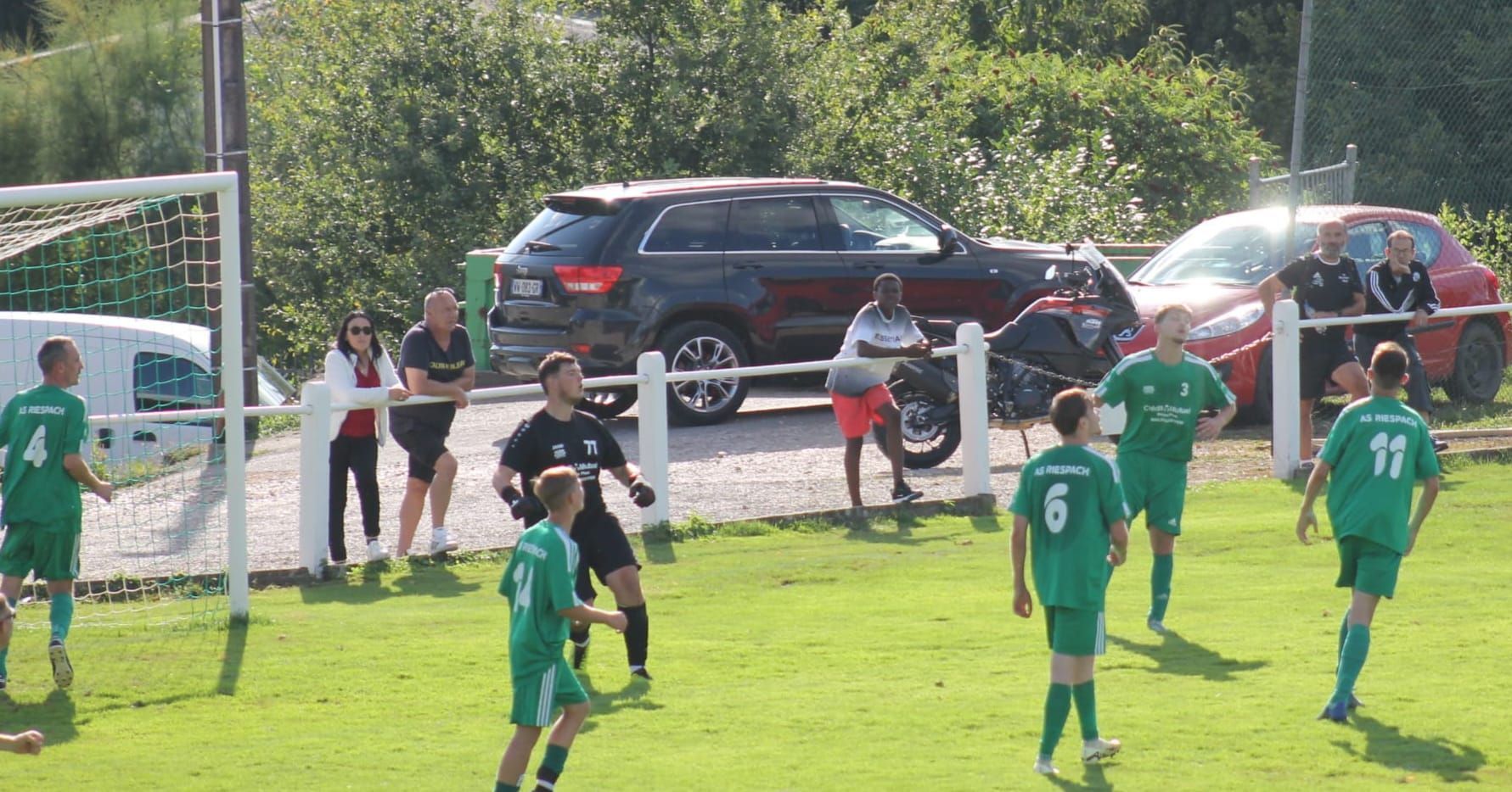 Un groupe de personnes joue au football sur un terrain avec des voitures garées en arrière-plan