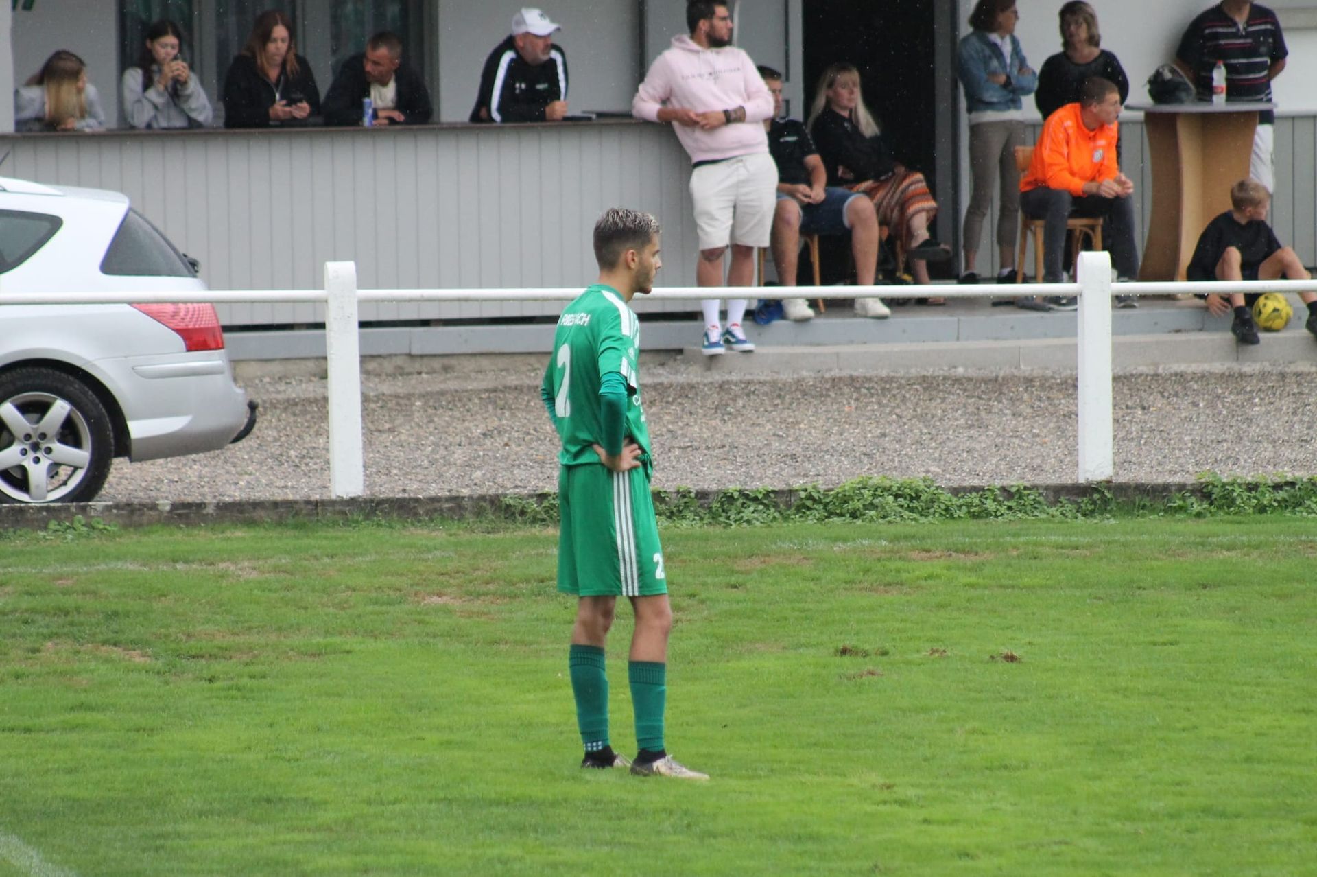 Un homme en maillot vert se tient debout sur un terrain de football.