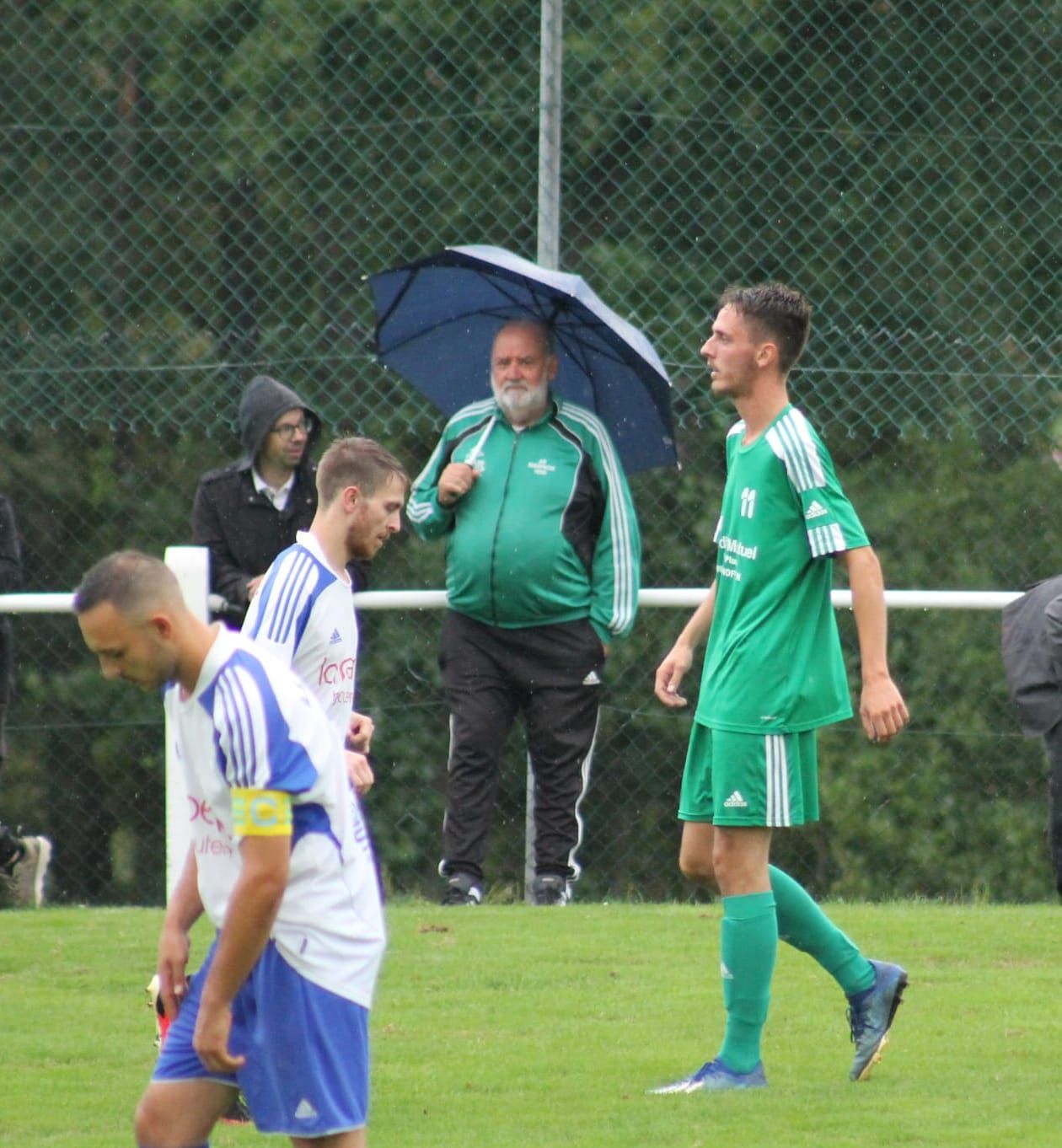 Un groupe de joueurs de football sur un terrain avec un homme tenant un parapluie