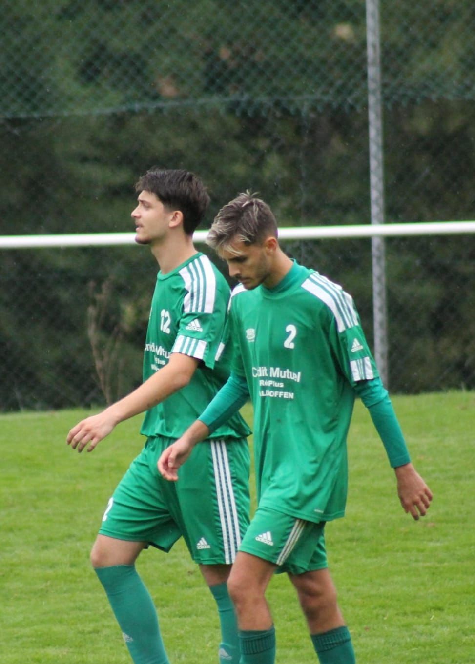 Deux joueurs de football en uniformes verts marchent sur un terrain
