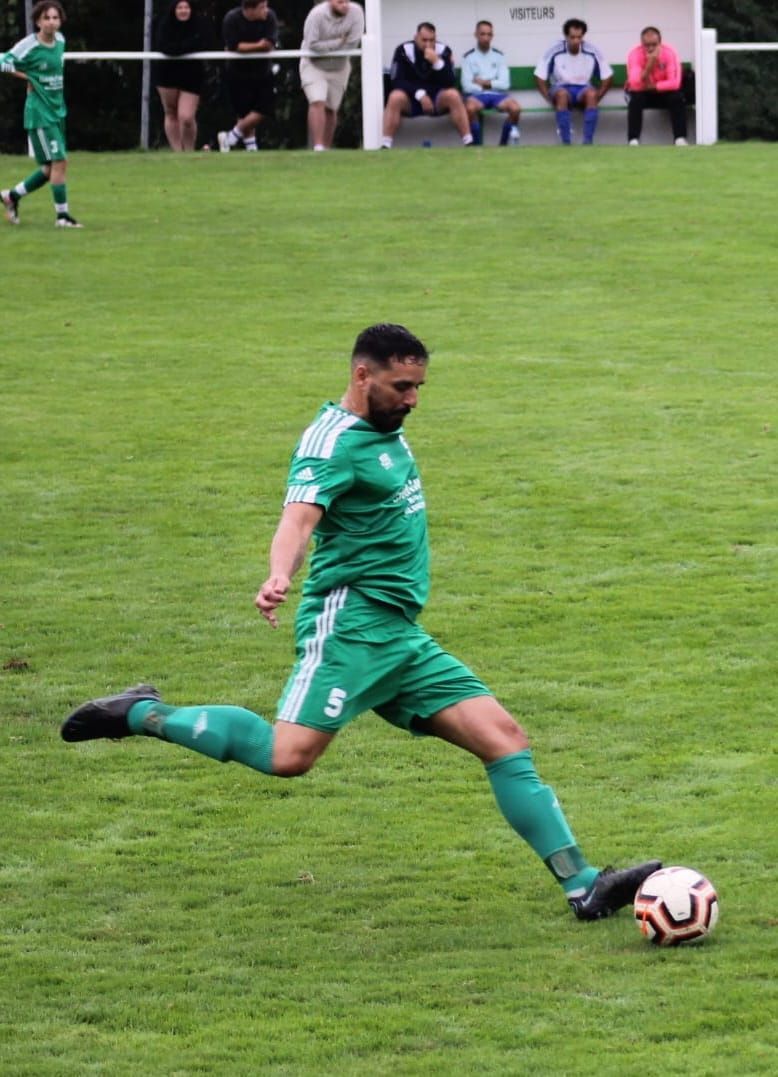 Un homme en maillot vert frappe un ballon de football sur un terrain.