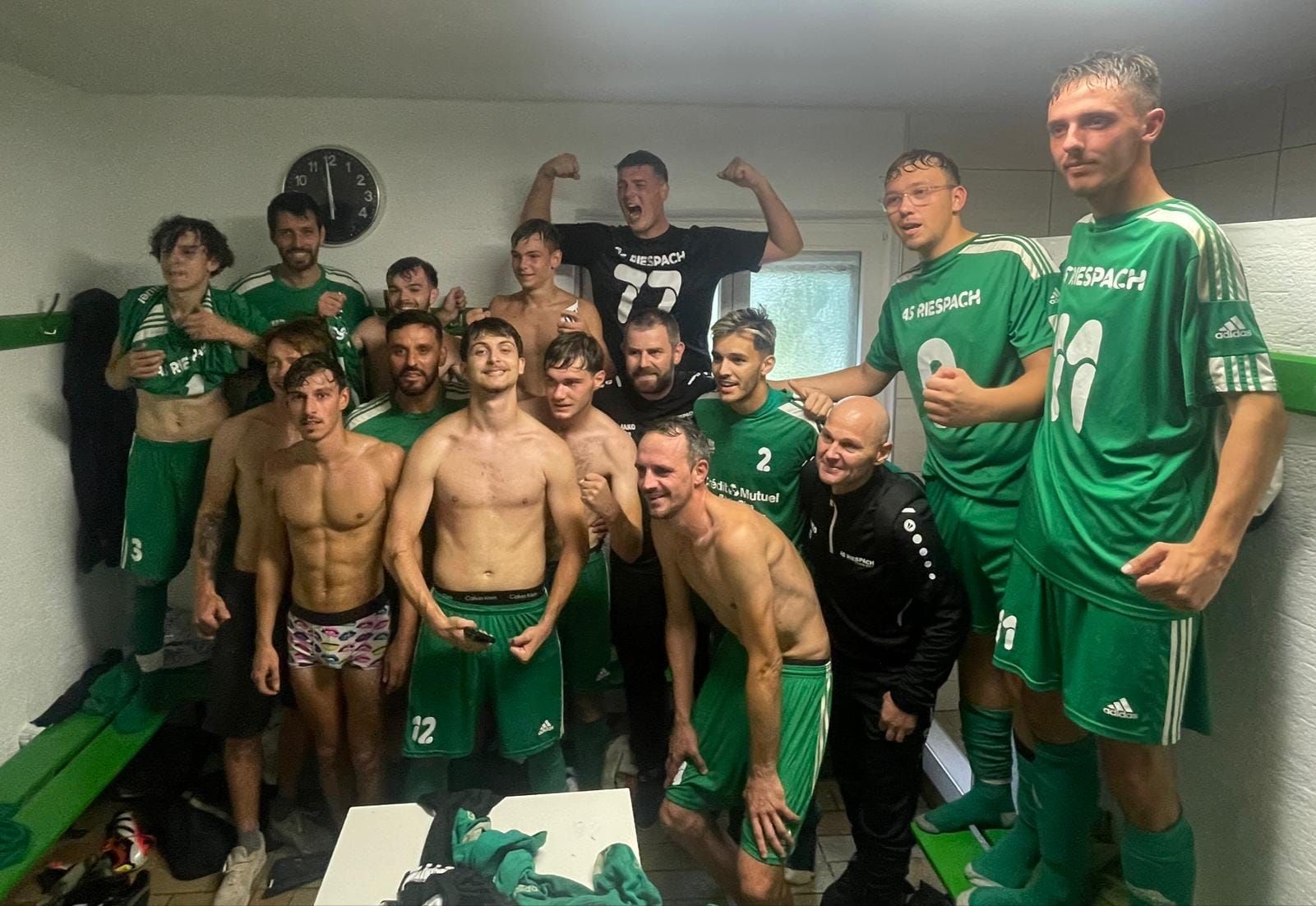 Un groupe d'hommes pose pour une photo dans un vestiaire.