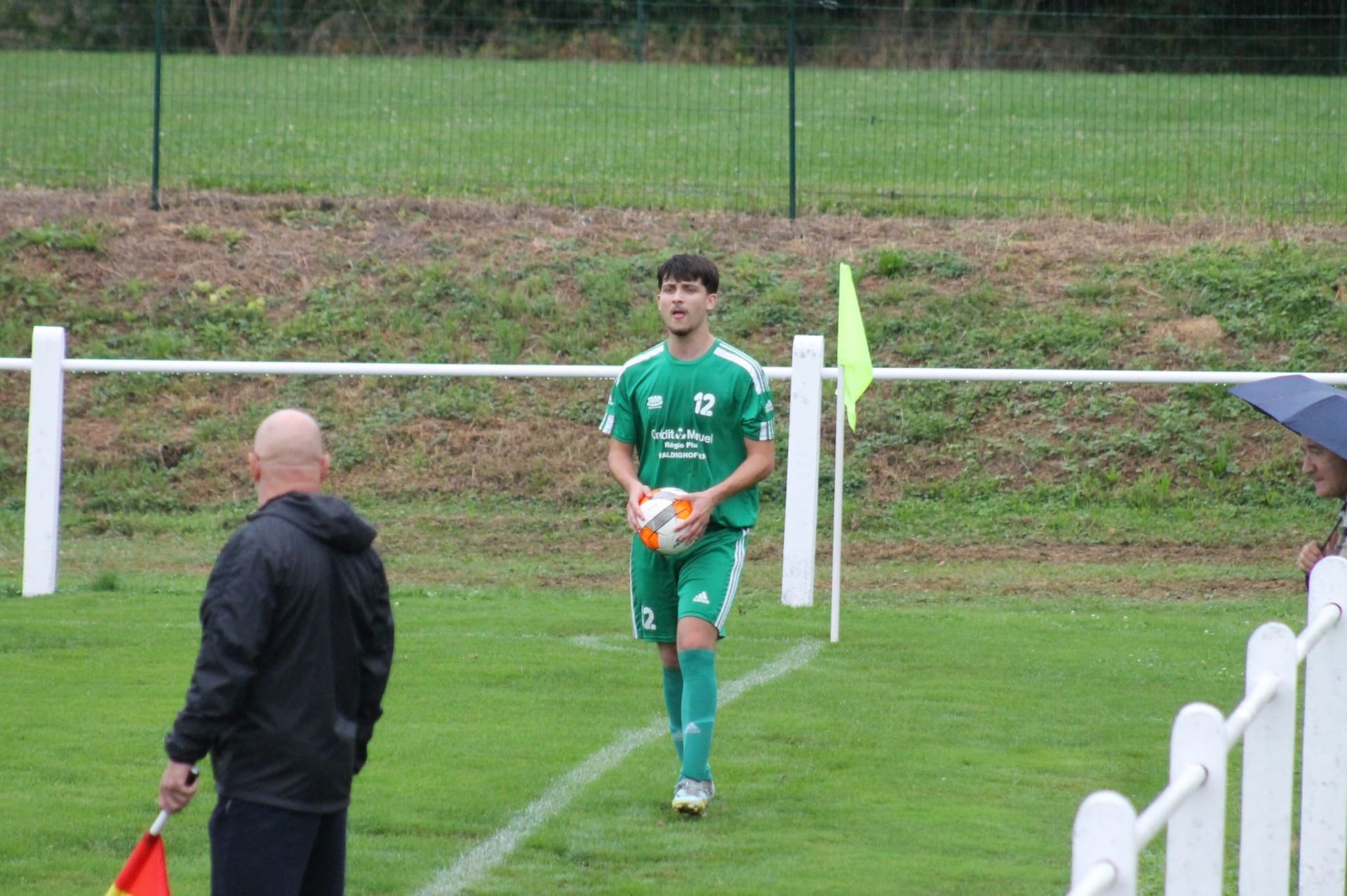 Un homme est debout sur un terrain de football tenant un ballon de football.