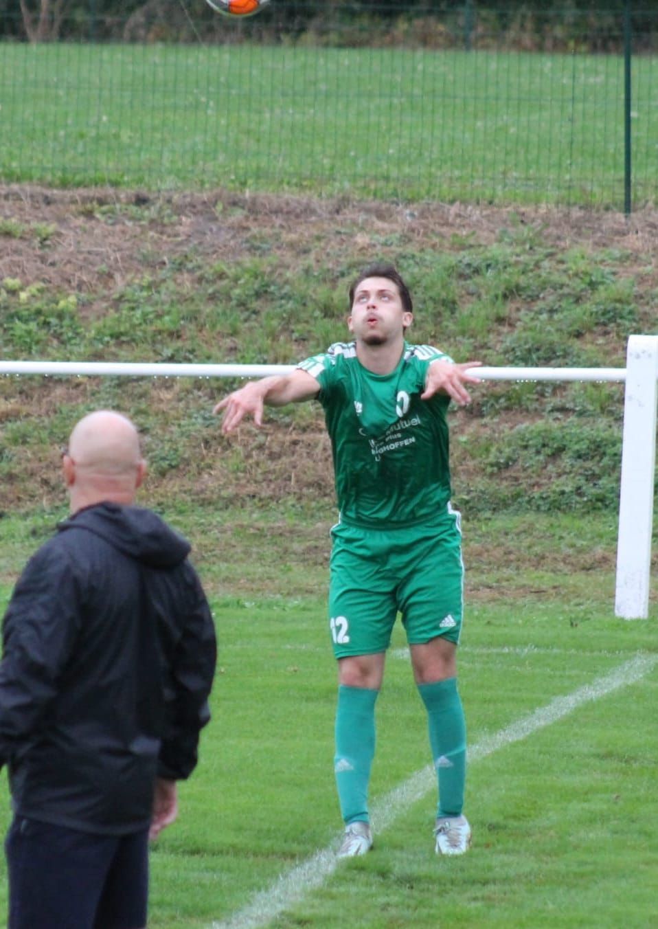 Un homme se tient debout sur un terrain de football et regarde un joueur de football lancer un ballon de football.
