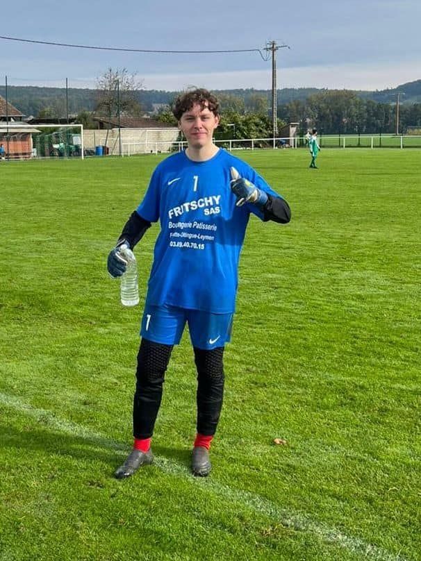 Un jeune homme se tient debout sur un terrain de football et tient une bouteille d'eau.
