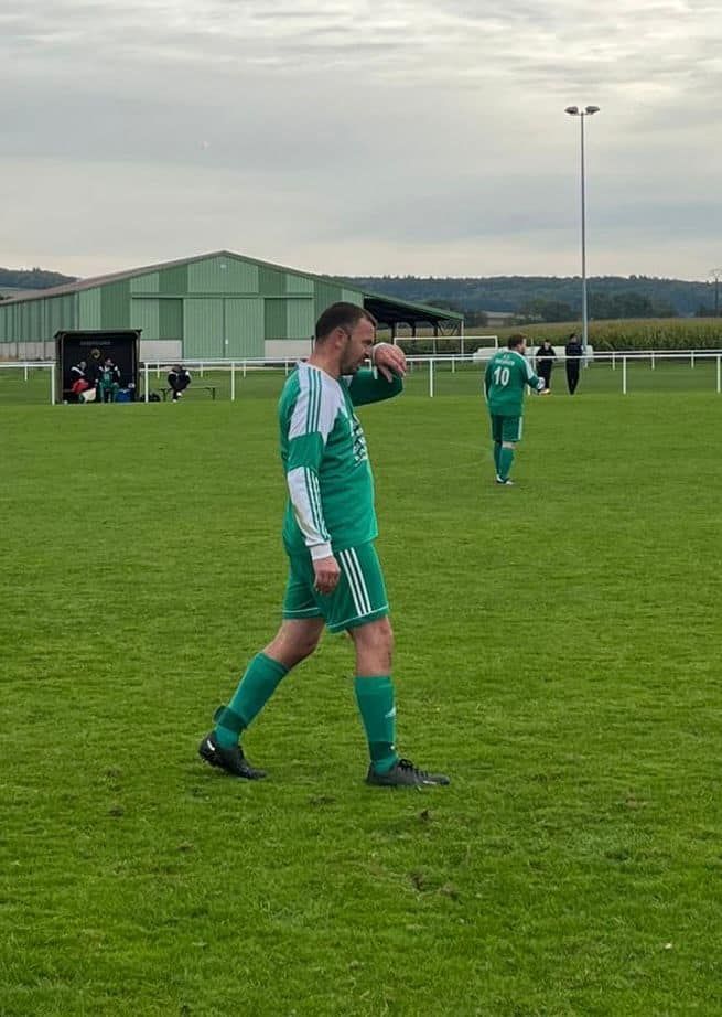 Un homme en maillot vert marche sur un terrain de football.