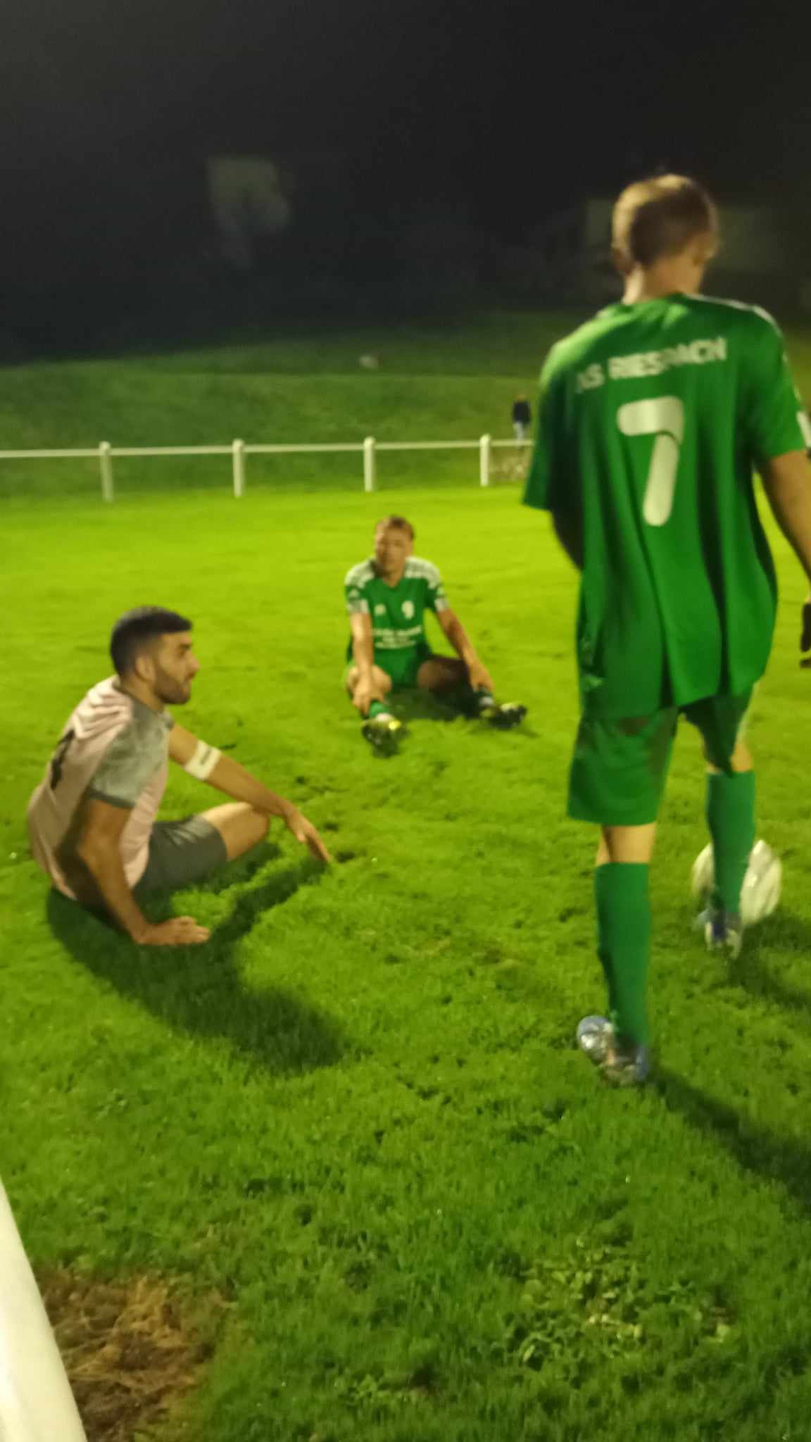 Un groupe d'hommes joue au football sur un terrain la nuit.