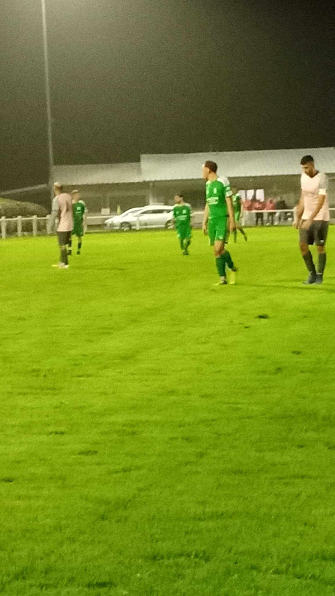 Un groupe de personnes joue au football sur un terrain la nuit.