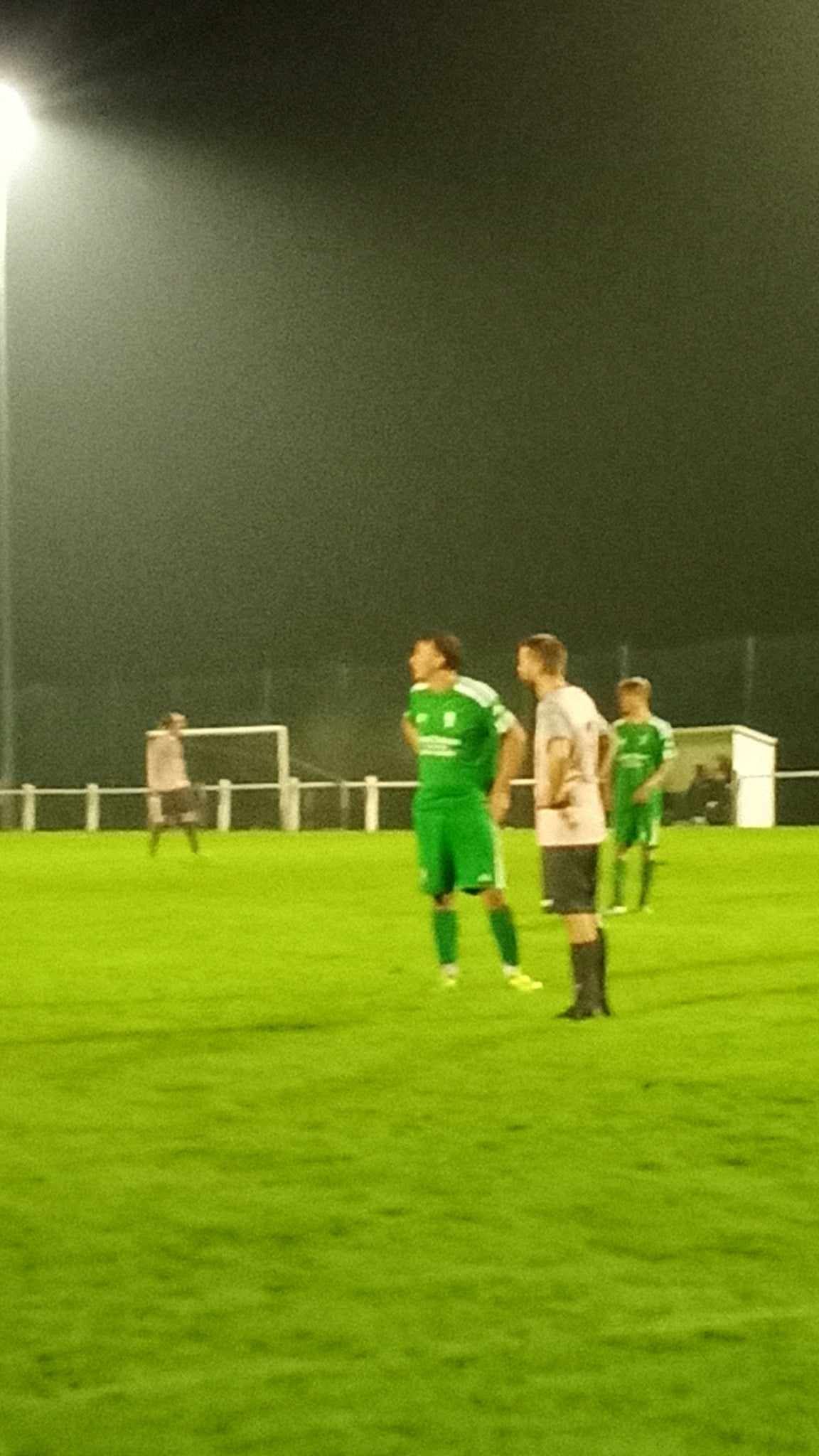 Un groupe de personnes joue au football sur un terrain la nuit.