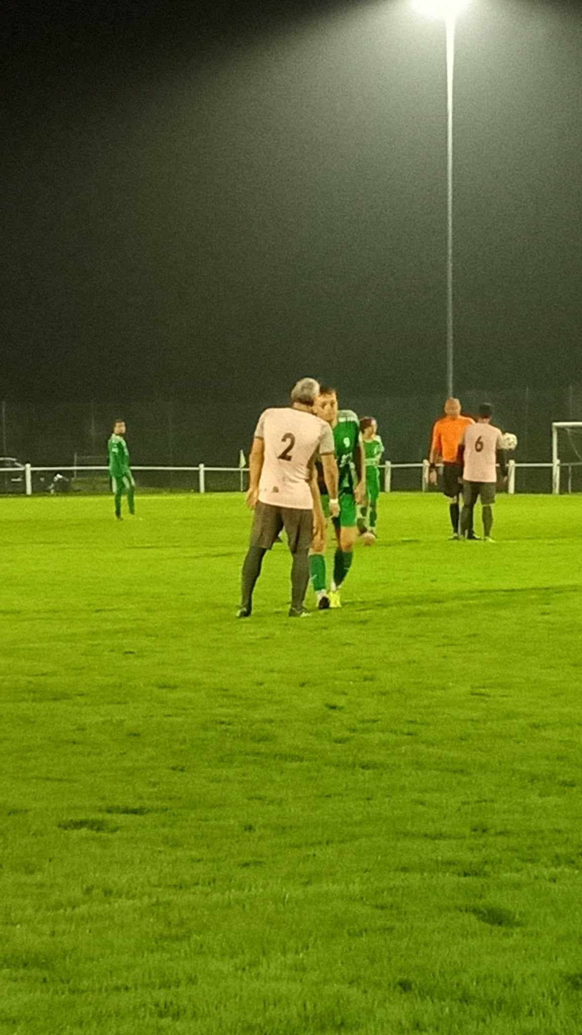Un groupe de personnes joue au football sur un terrain la nuit.