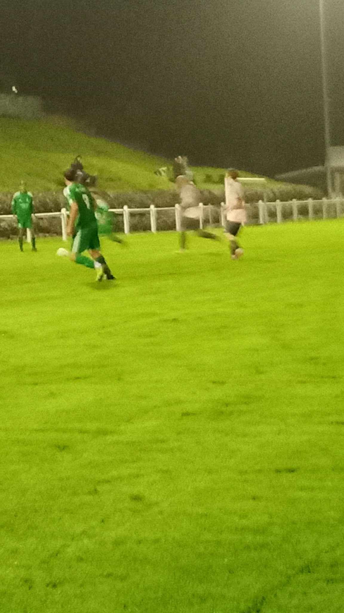 Un groupe de personnes joue au football sur un terrain la nuit.