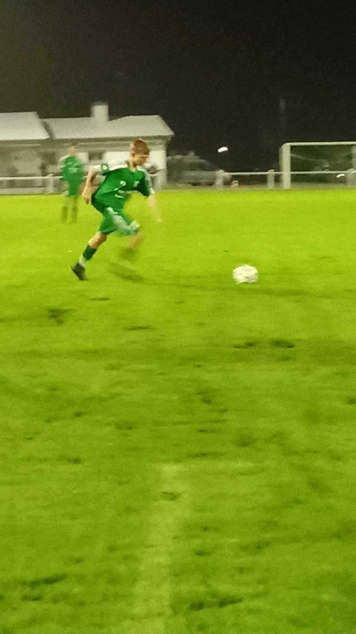 Un joueur de football en uniforme vert frappe un ballon de football sur un terrain.